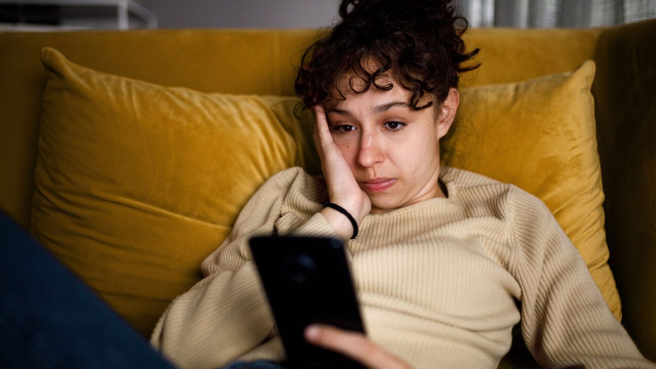 A young female sitting on a couch looking at a smartphone.