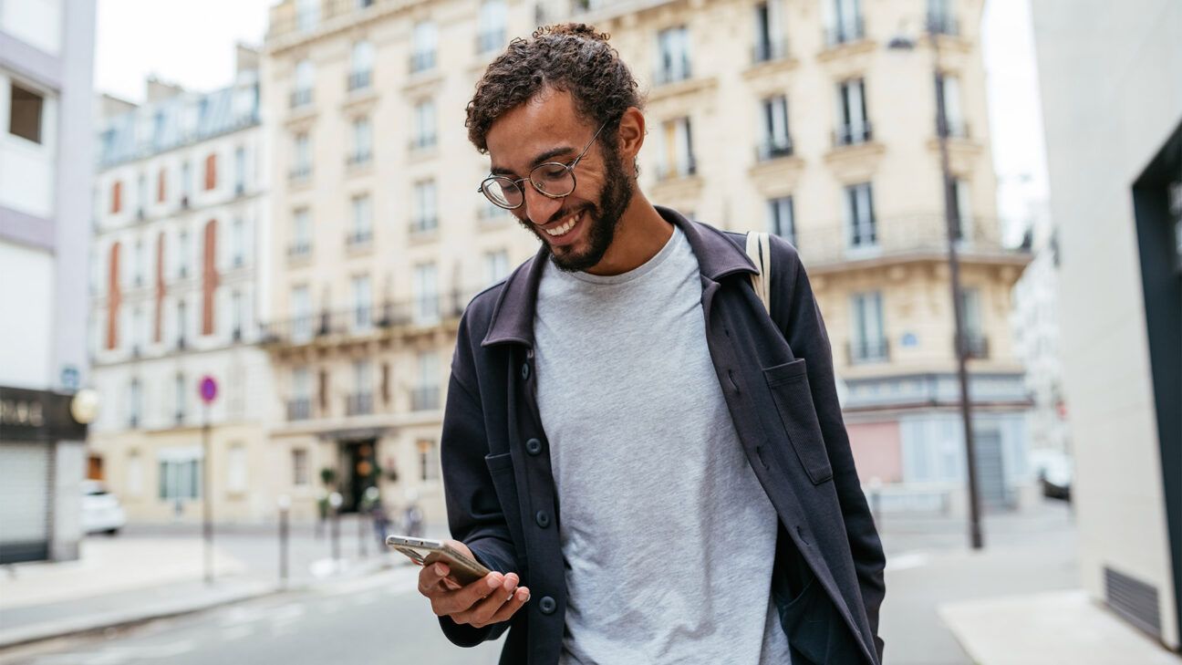 A happy male looking at a smartphone outside.