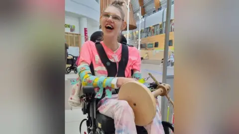 Peter Crowe A picture of Taylor Crowe in her wheelchair, smiling 