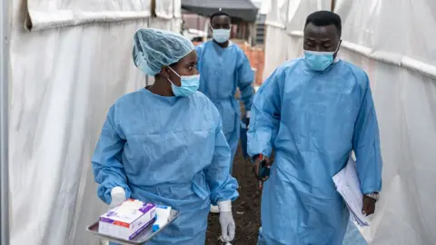 Getty Images Health workers wearing masks and scrubs chat as they walk in between tents at the Munigi mpox treatment centre in North Kivu, DR Congo on 17 August