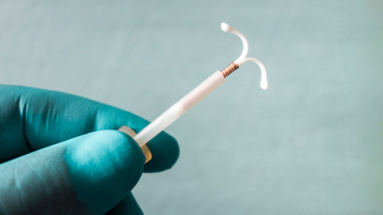 A gloved hand holding an IUD device.