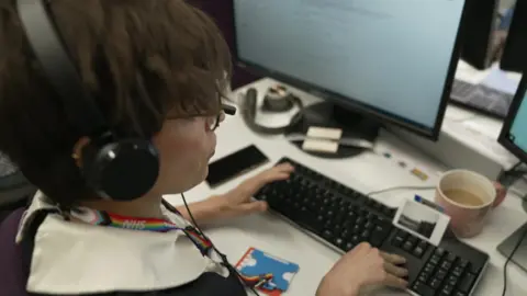 BBC One of the trained counsellors, Chris, wearing a headset at her computer