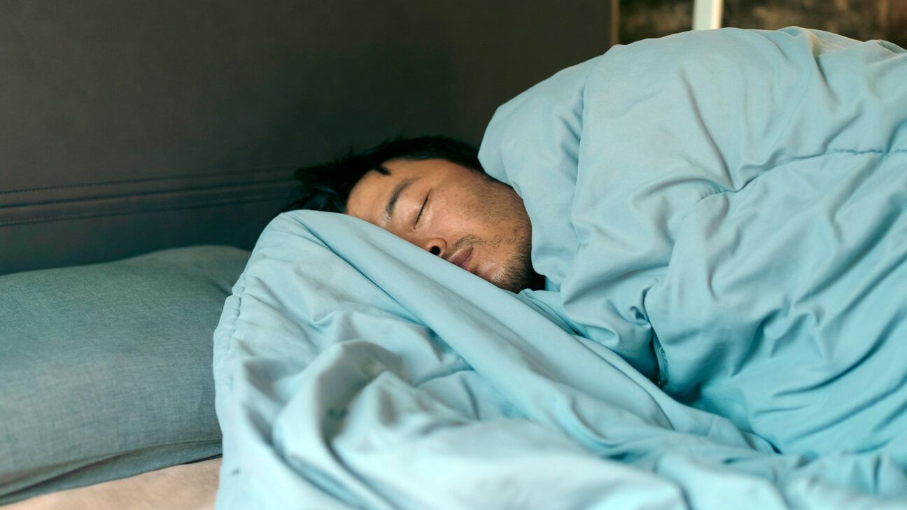 Male wrapped in a blue blanket asleep in a bed