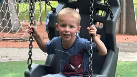 Andrew Gwynne Lyle, now aged five, sits on a swing