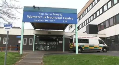 A hospital entrance with a sign to the neonatal ward. An ambulance is parked outside