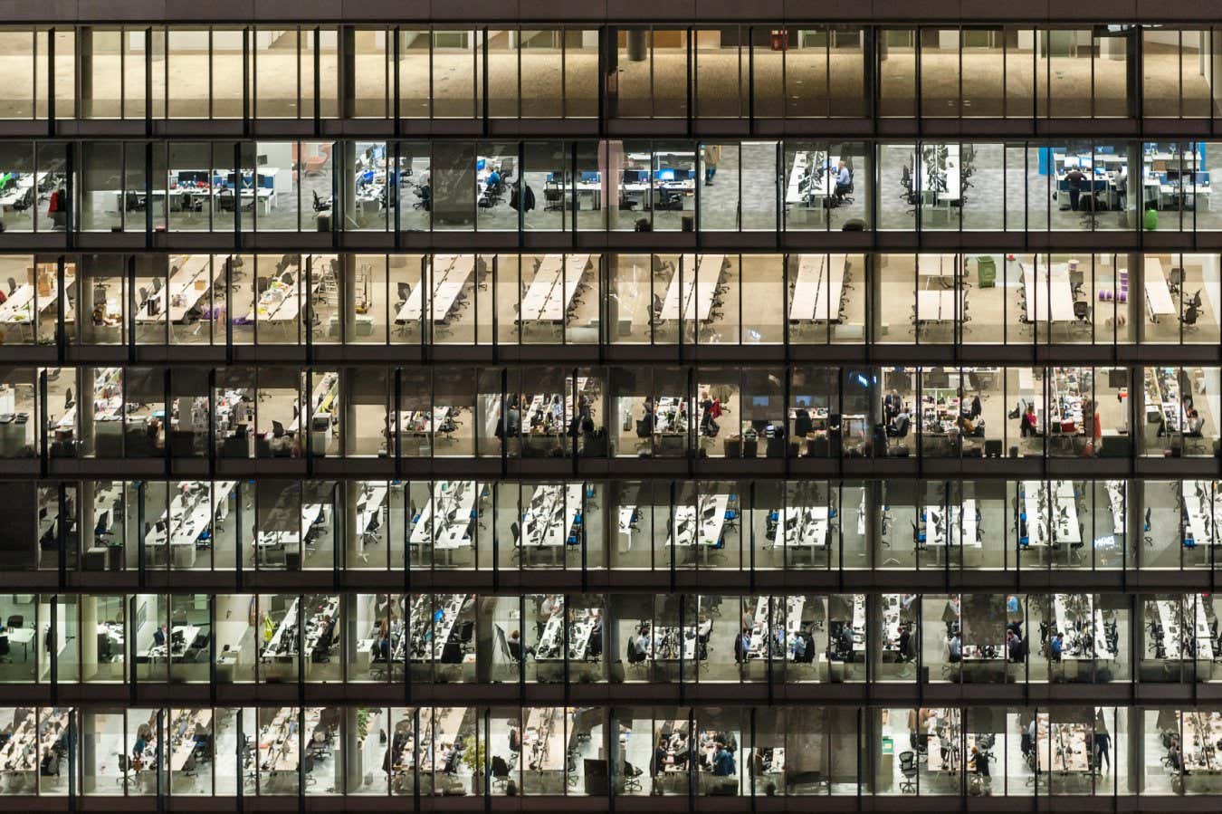 RD3GJW London, UK. Office workers at night, seen through the windows of an office block in the City, London's financial district