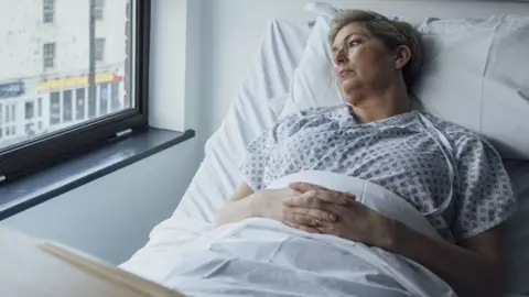 Getty Images A woman lies in a hospital bed and looks out of a window