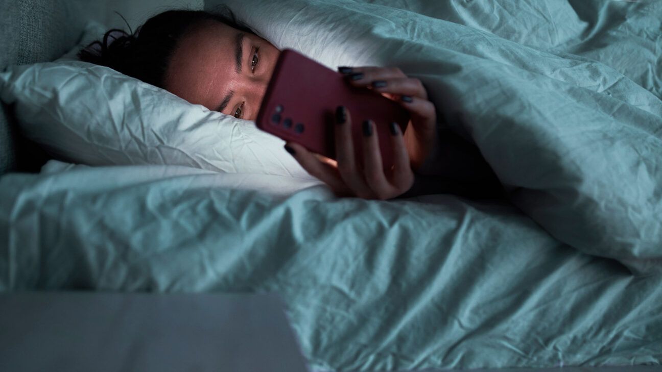 A female in bed looking at a smartphone.