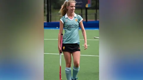 Clarissa's Campaign Clarissa Nicholls playing hockey at university. Miss Nicholls is wearing a light blue, short-sleeved, shirt bearing with the word 