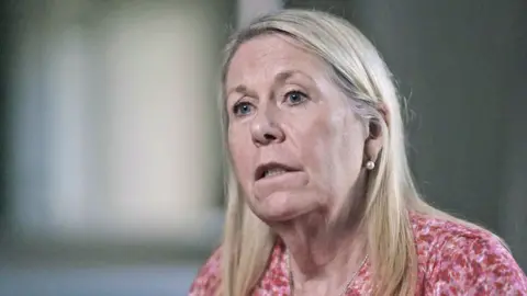 Head and shoulders shot of Dr Sandie Bohin - with straight blond hair and a pink and red patterned top.  