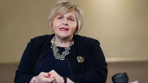 PA Media Donna Ockenden, wearing a dark business suit, speaking at a press conference.