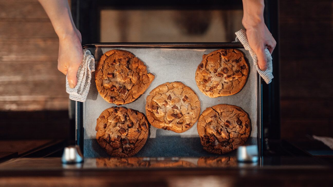 A person holding a baking sheet of cookies.