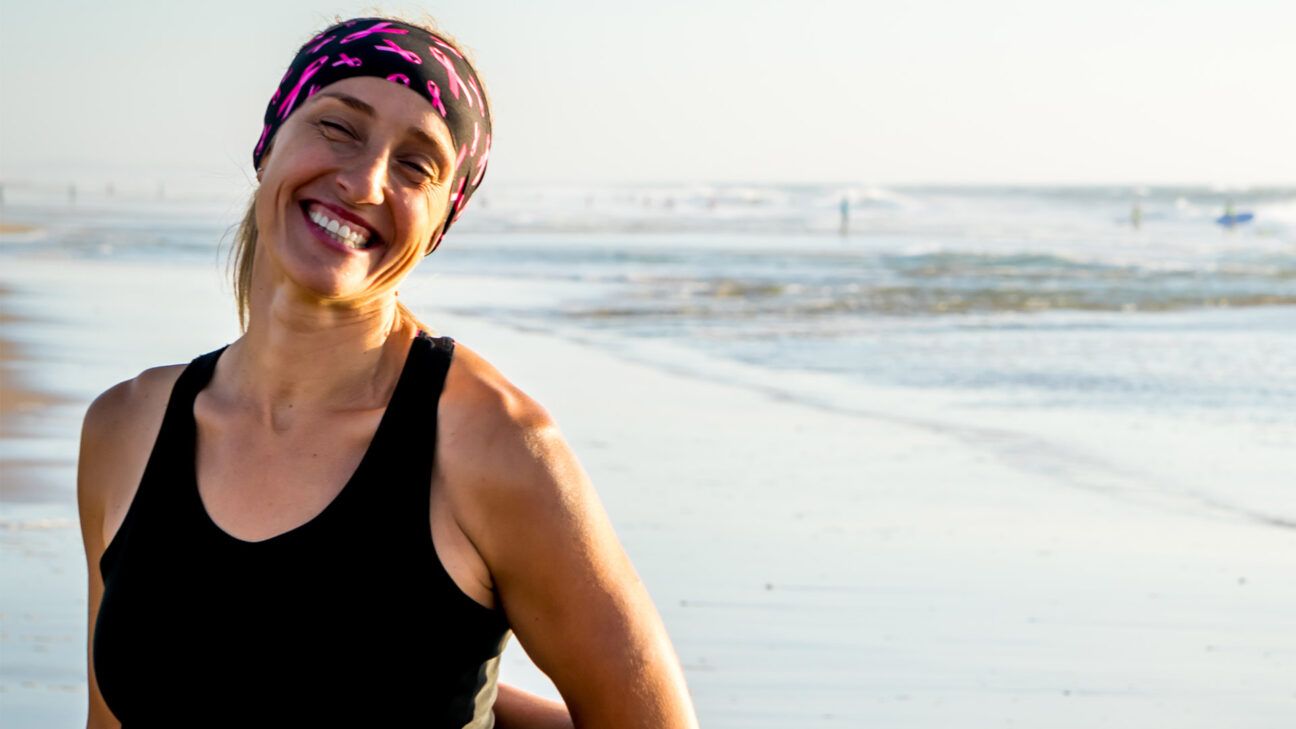 a smiling woman wearing breast cancer awareness headband with pink ribbons at a beach