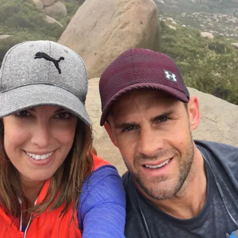 Andrea Byrne / Y Lolfa Andrea, wearing a grey baseball cap while hiking, smiles for a selfie next to husband Lee, who is wearing a maroon baseball cap