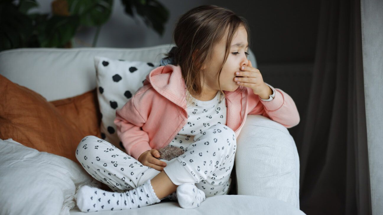 Young female child covers her mouth coughing