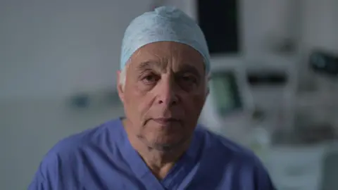 BBC/Adam Walker Consultant anaesthetist Richard Marks is photographed in a hospital environment, wearing his dark blue scrubs and pale blue surgeon's cap.