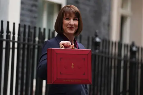 PA Media Chancellor of the Exchequer, Rachel Reeves holding up. red budget box in Downing Street