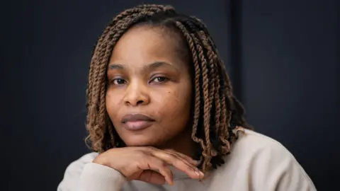 PA Media Ruvimbo Kaviya - a woman of about 40 with braided hair and a cream top. She is looking into the camera with her hand placed beneath her chin.