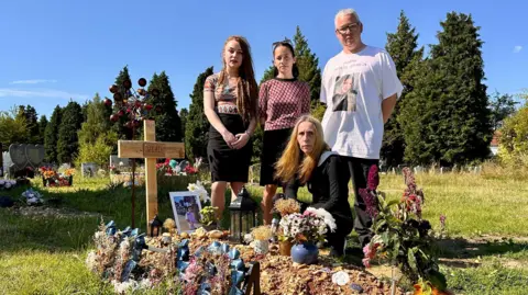 Vlad's family, Mia, Masha, Anna & Graham at his graveside in Southampton which is covered in tributes and marked by a home made wooden cross with his name on