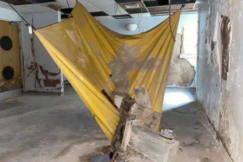 A yellow piece of material is pictured to capture dust and floodwater inside an abandoned hospital building