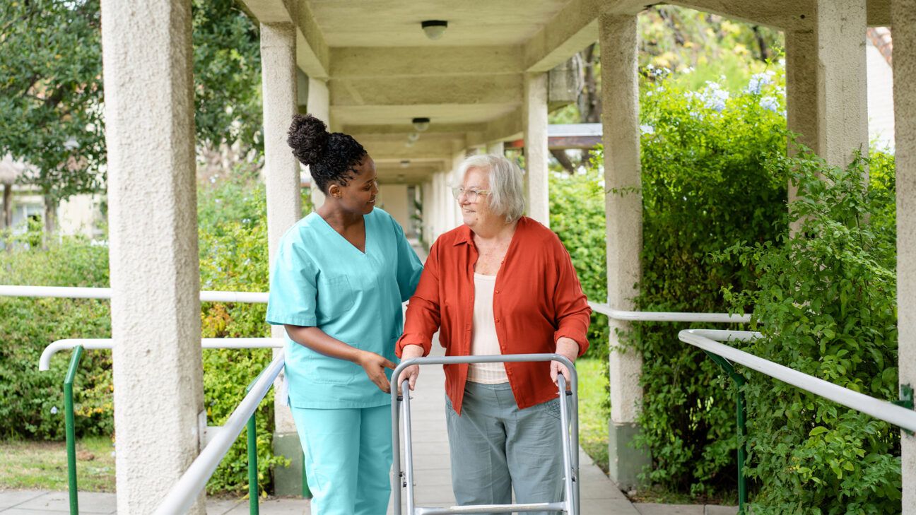 Nurse helps older female recovering from stroke walking outdoors