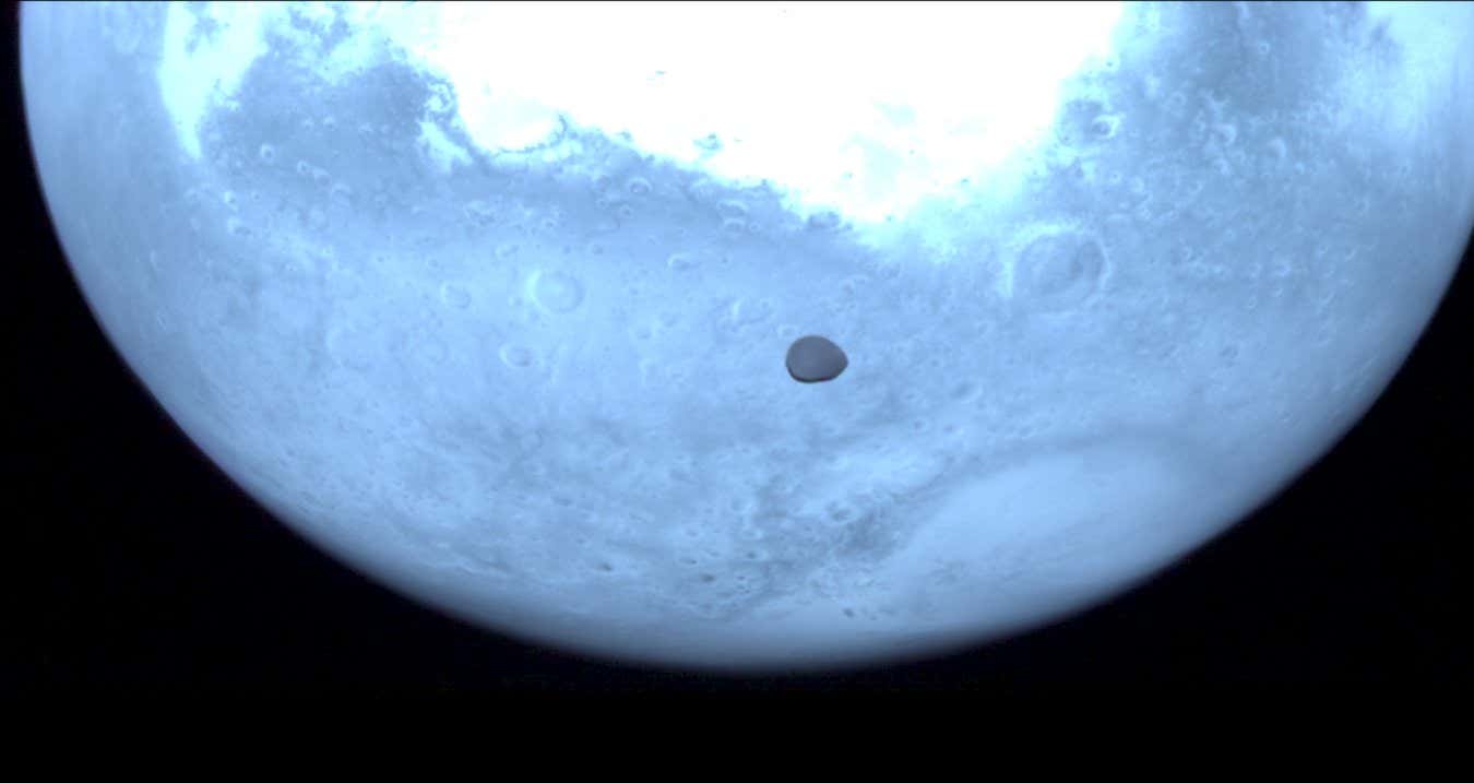 Mars appears light blue in this near-infrared image from the Hera spacecraft, with its moon Deimos represented by a dark mark towards the centre of the image