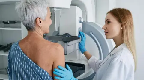 Getty Images A woman goes for a mammogram. She is pictured alongside a female medical professional.