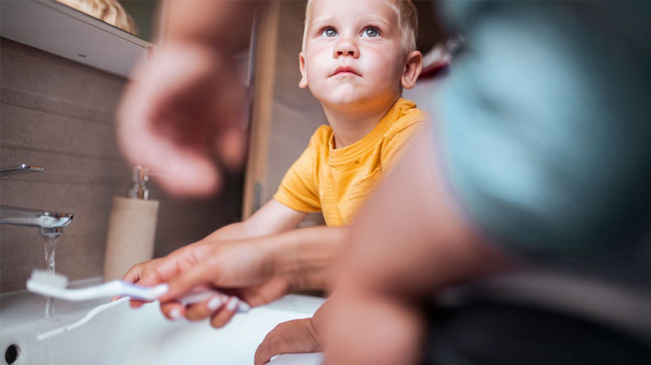 A young child brushes his teeth with a caregiver