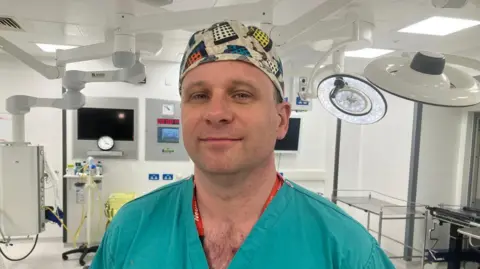 BBC A man in green surgical scrubs and cap with daleks on it in an operating theatre