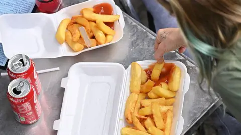 Getty Images Close up cartons of chips and fizzy drinks and a hand holding a chip and dunking it in ketchup 