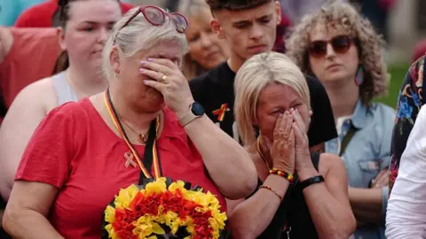 PA Two women, part of a group who held a minute's silence in May 2024 in memory of people who died because of the infected blood scandal. They are covering their faces with their hands in grief.