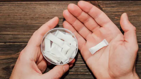 Getty Images A pair of hands holding a can of pouches in one hand and a single pouch in the other. Pouches are white sachets.