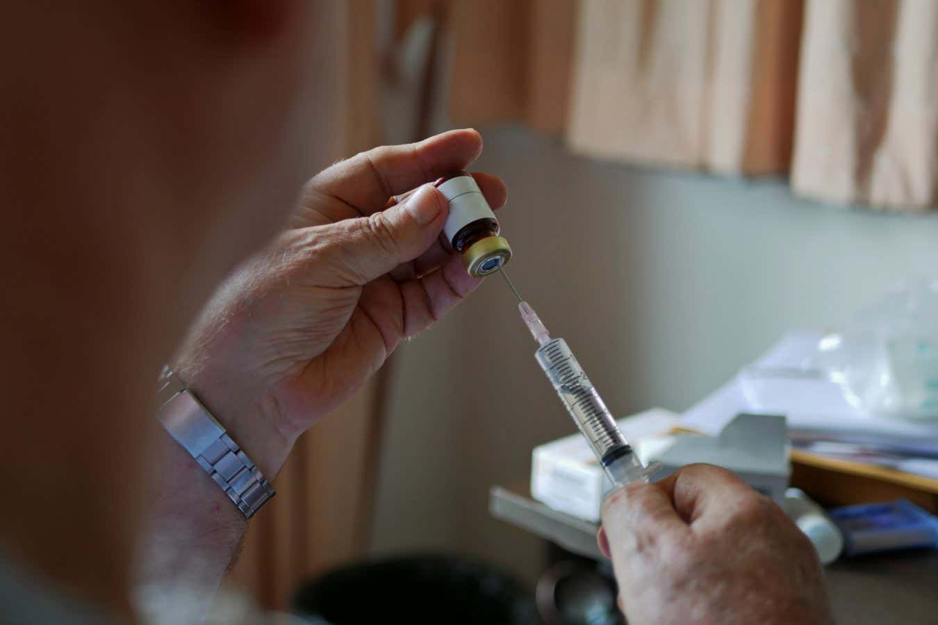 An old man's hands carefully pulling the medicine into the syringe by himself at home - self injecting in the elderly