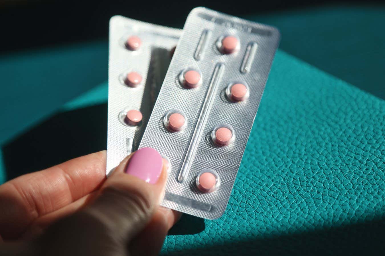 Women's Health. Female Contraception Estrogen Hormones. Hormone Replacement Therapy. Silver Colored Blister Pack With Small Pink Pills Against Blurred Female's Hand Using Phone. Ambient Light, Copy Space