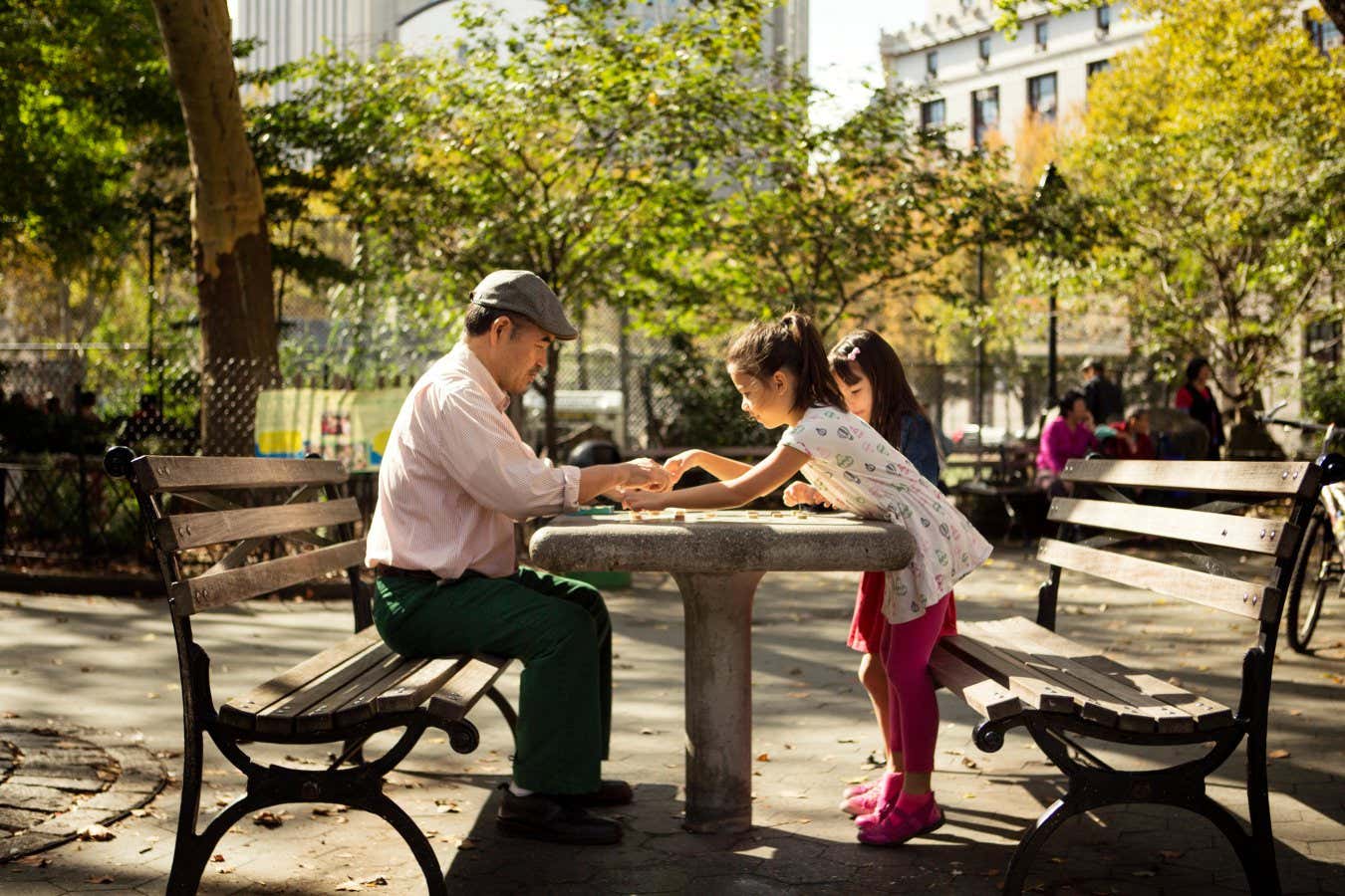 An older man playing checkers game with children at a park table