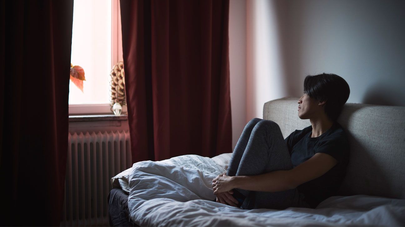 Young male sits on bed and gazes out window