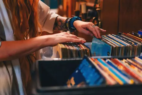 Getty Images A close up of the arms of a woman flicking through a box of colourful record albums in a record shop