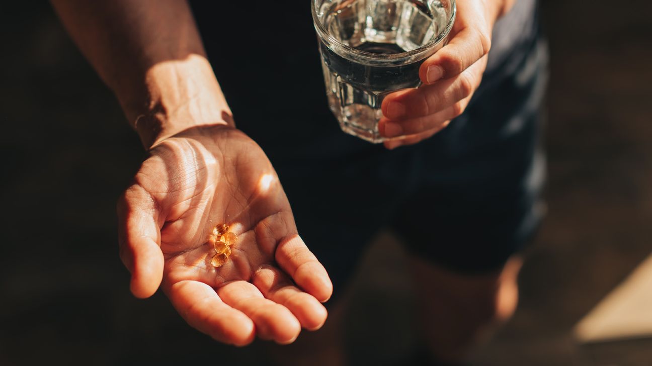 Vitamins in hand with glass of water