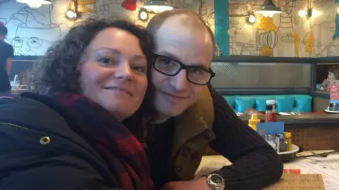 Emma Harley Emma Harley sits next to her brother Terry White at a table in a restaurant. Both are wearing dark tops. Emma has dark curly hair and wears a dark blue and red scarf. Terry wears dark rimmed glasses and a silver wristwatch. Both are smiling at the camera