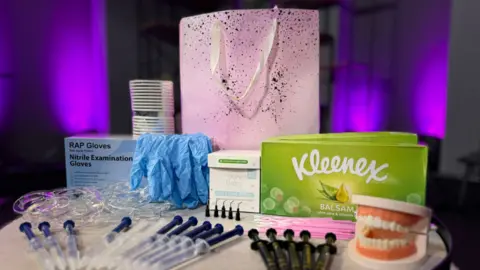 A teeth-whitening kit containing syringes of chemicals, rubber gloves, cotton buds, tissues, a pair of false teeth to practise on, and the pink, sparkly bag in which it all came.