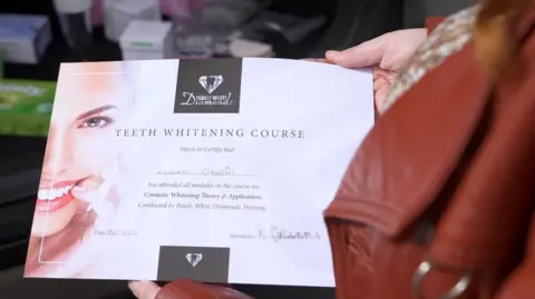 A certificate from Pearly White Diamonds, being held by our undercover reporter. On the left-hand side is the right-hand side of a woman's face, bearing a big grin, and on the remainder of the certificate the following is written: