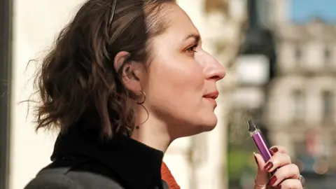 Getty Images A young woman with sunglasses vaping in the street