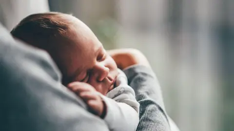 Getty Images A baby lies asleep in its carers arms. 