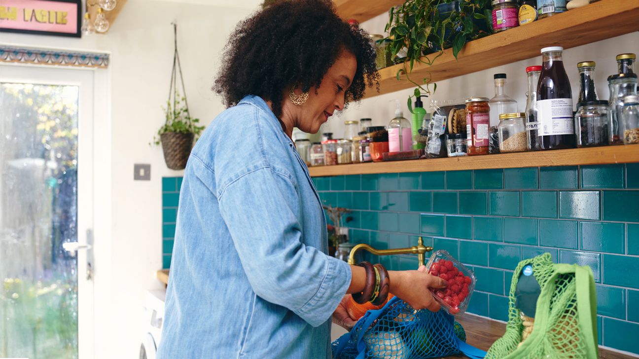Menopausal female unpacking fruits, vegetables from grocery bags in kitchen