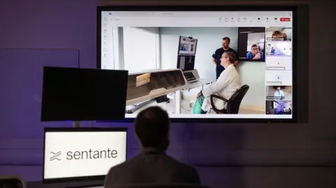 University of Dundee A man watches a big screen, where a medic is carrying out a procedure.