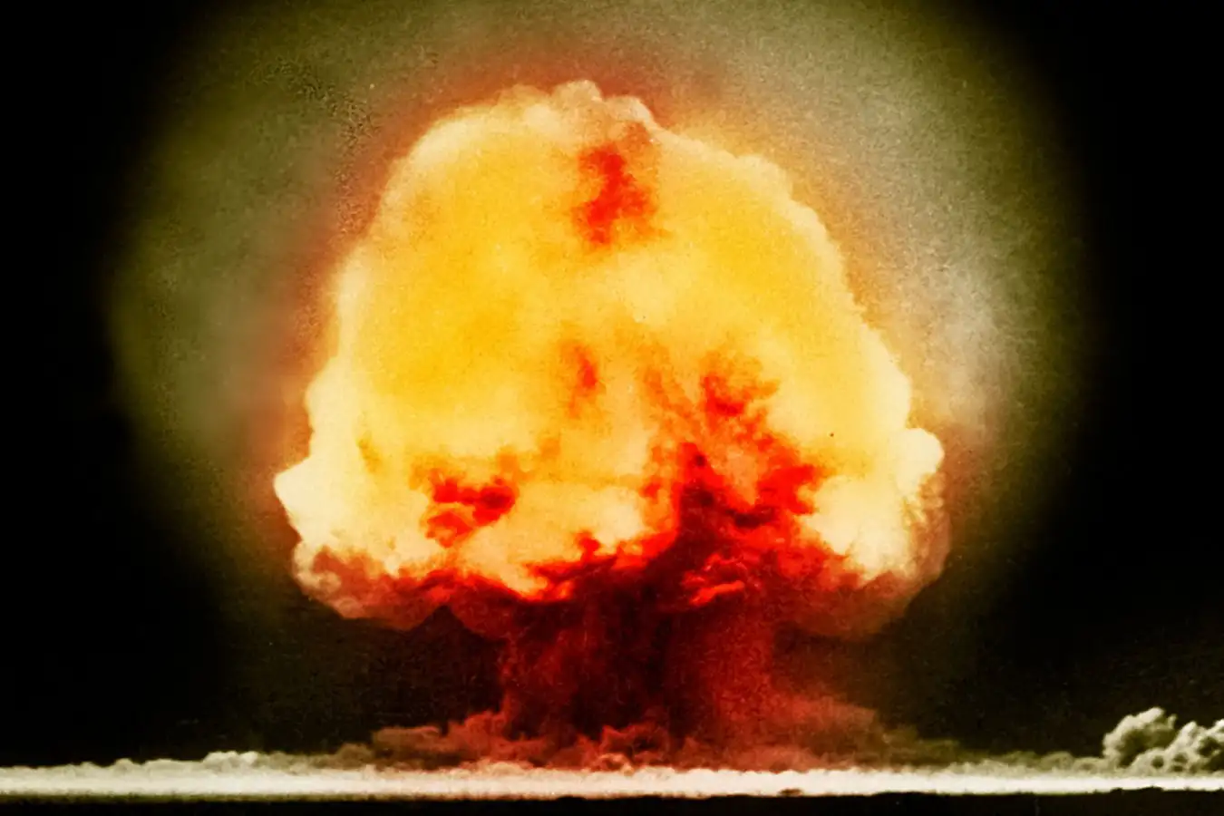 A bright, orange mushroom cloud over desert sand in New Mexico