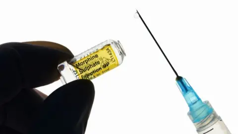 Getty Images Stock image of a gloved hand holding 10mg liquid morphine sulphate glass vial and syringe.