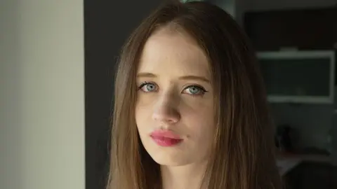 BBC A portrait of Viktoria, a young woman with long, brown hair and blue eyes, pictured close-up and facing the camera