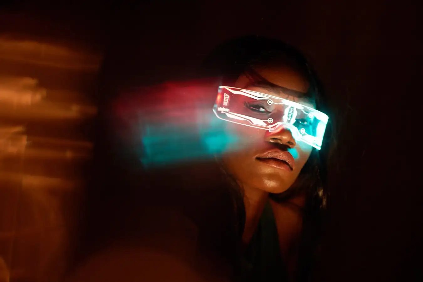 A futuristic depiction of a woman wearing neon light-up augmented reality glasses. The glasses emit blue and red lights, creating a cyberpunk atmosphere. The young Black woman is captured in a dark environment with dynamic light streaks, emphasizing the high-tech and futuristic theme.