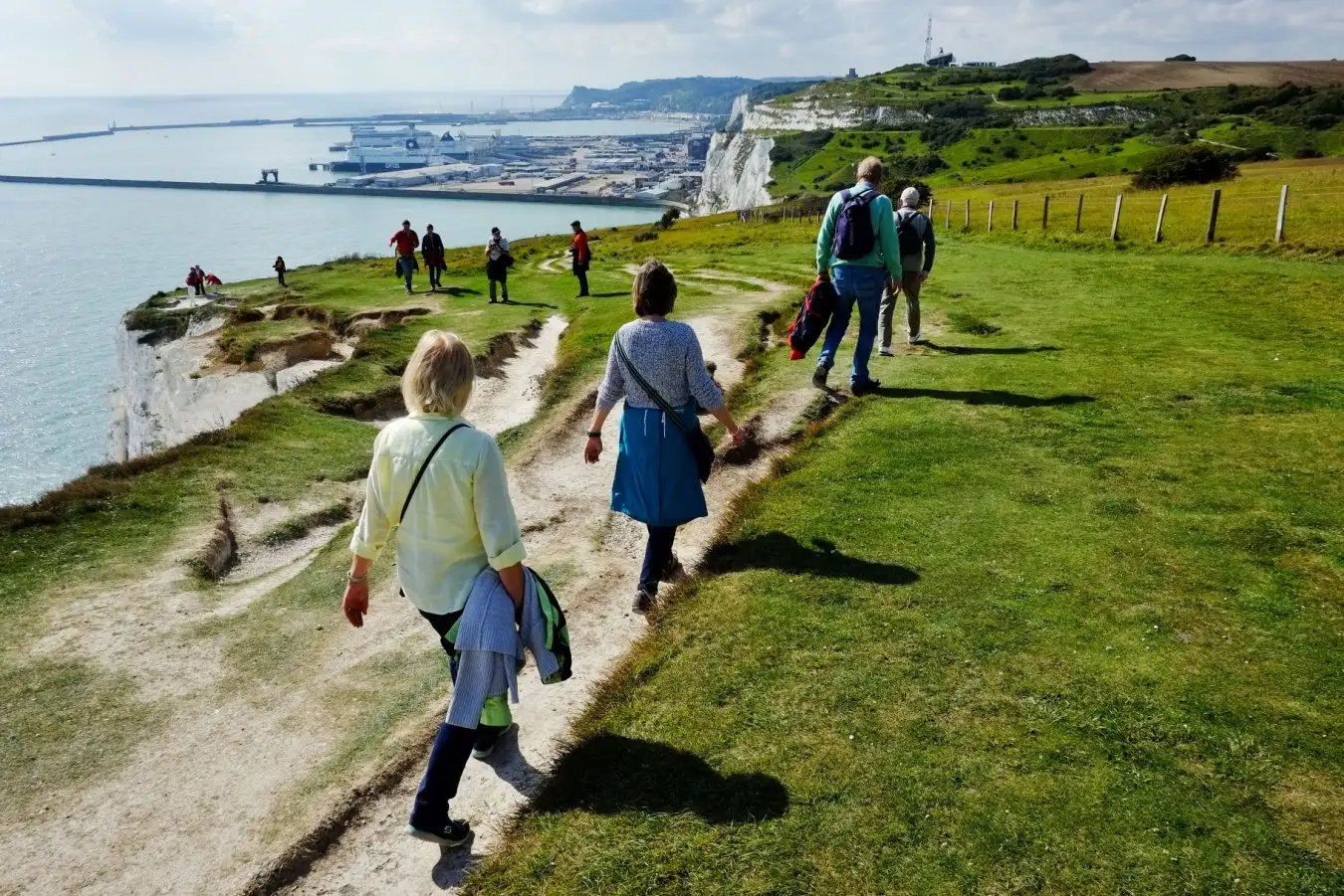 People walking along the cliff tops with a harbour in the distance. Dover, England,